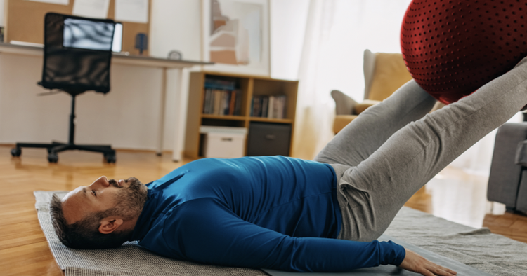 Man lying on his back lifts red exercise ball with his legs