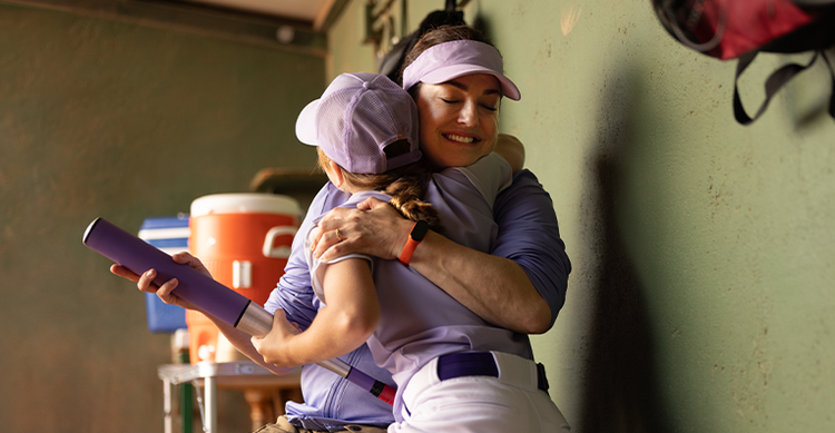 Softball coach hugs Little League player in the dugout